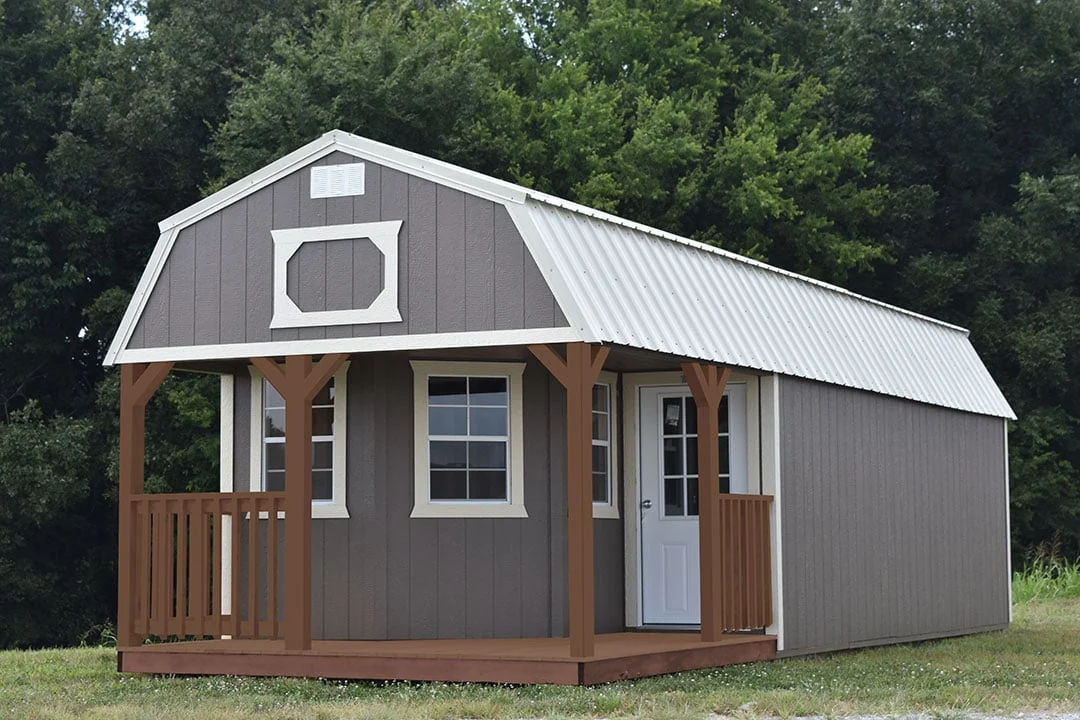 Derksen cabin style example with a wood porch and gray siding in a wooded setting